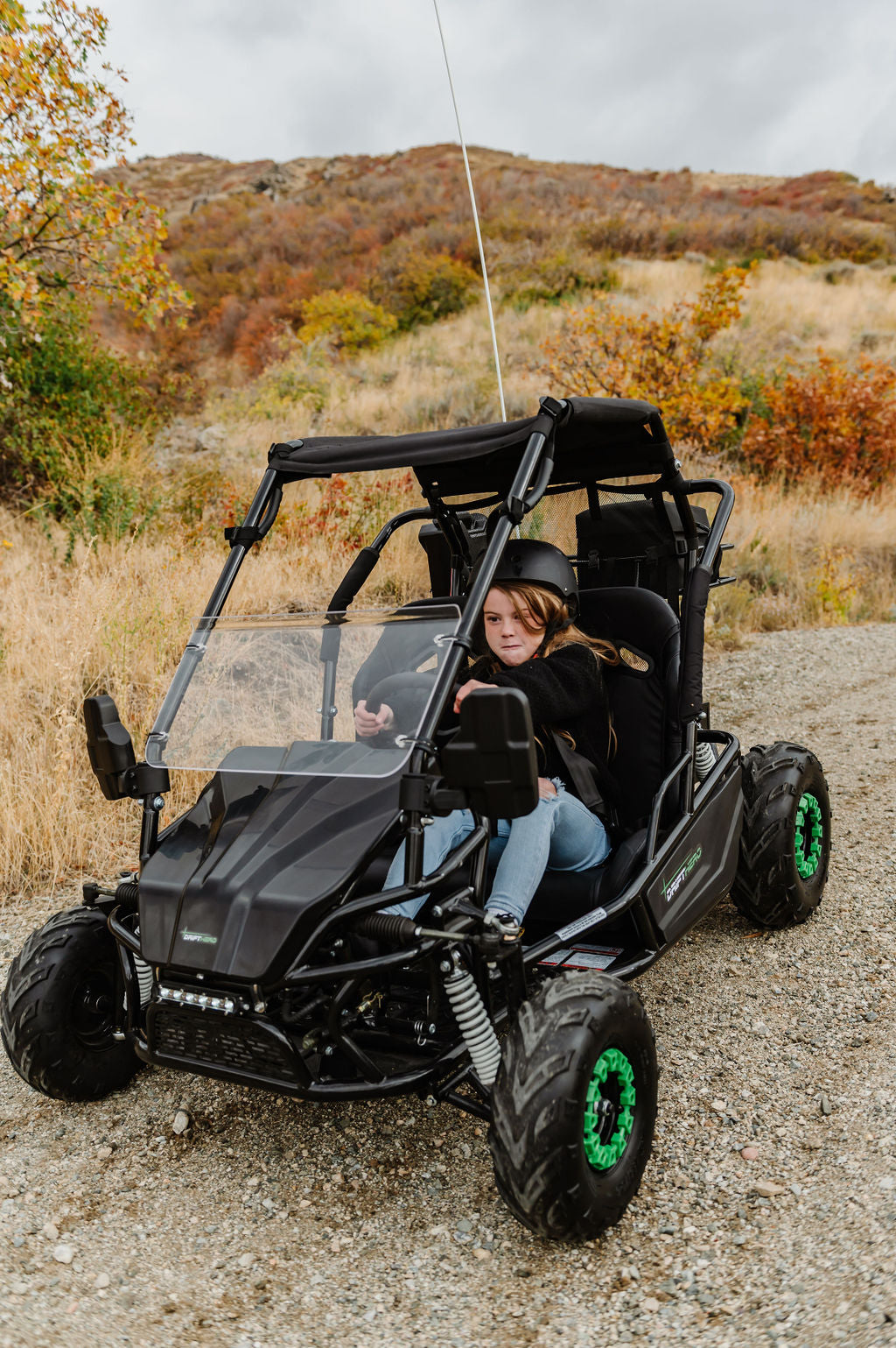 Young rider wearing a helmet driving the Drift Hero 2-seat electric go-kart on a gravel trail