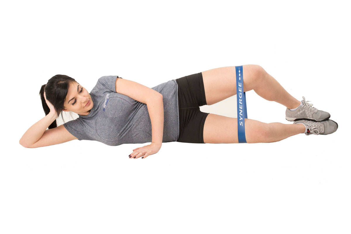A person using a Synergee Mini Band around the thighs for a leg exercise